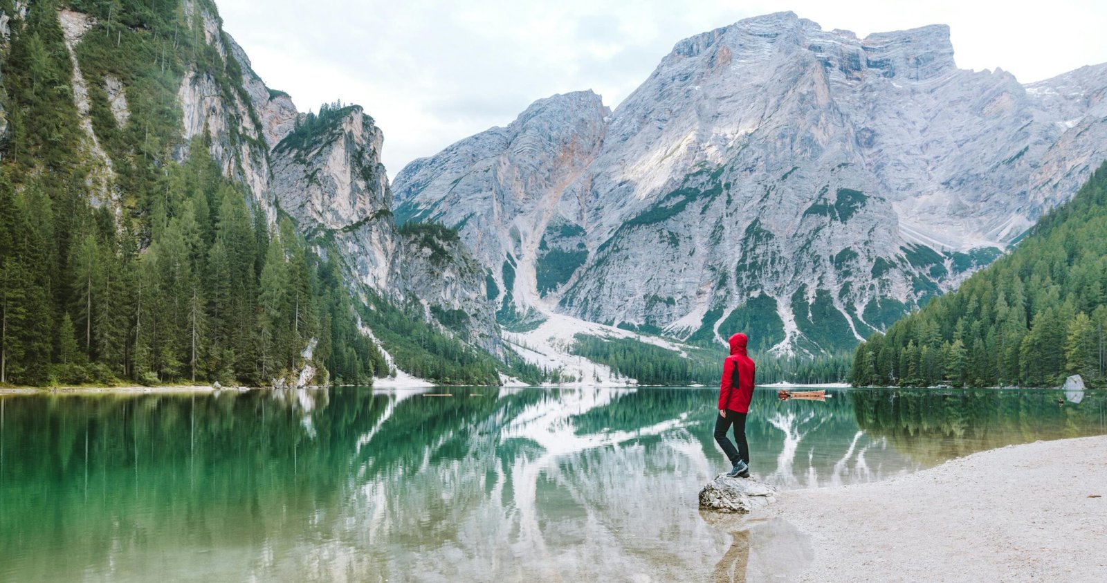 Man Wearing Red Hoodie Standing Near Body of Water With View of Mountains